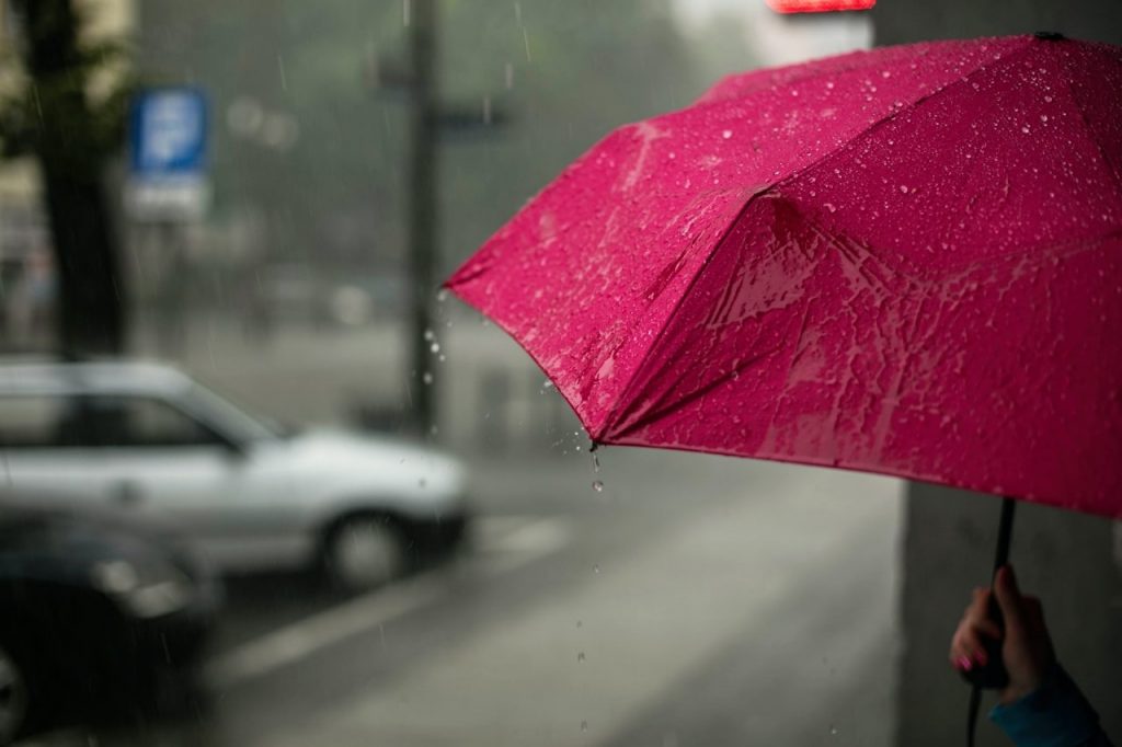 Personal injury attorney in Rancho Cucamonga holding red umbrella on rainy Rancho Cucamonga city street.